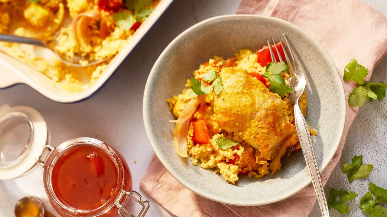 A speckled bowl, sitting on a pin napkin on a textured surface, holds a serve of a bright chicken and couscous dish. A