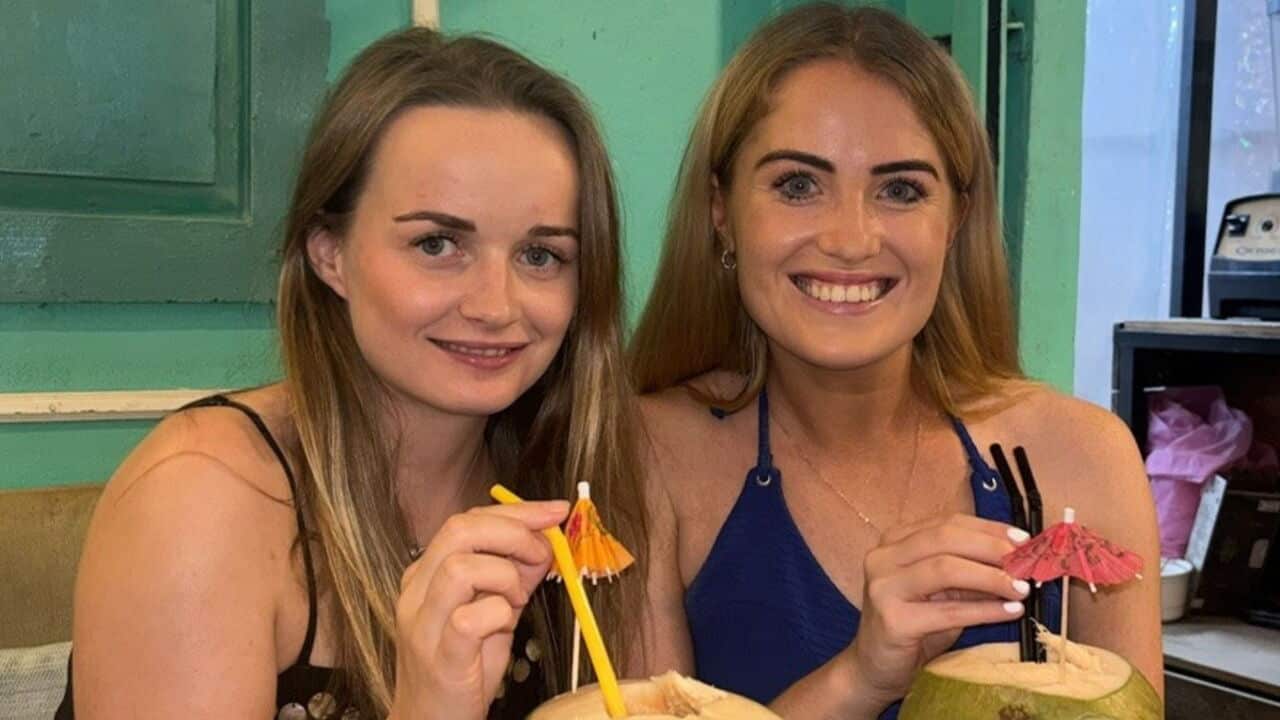 closeup of two young blonde women drinking from coconuts in a bar with blue background
