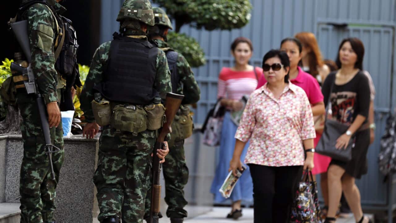 Thai office workers walk past armed soldiers
