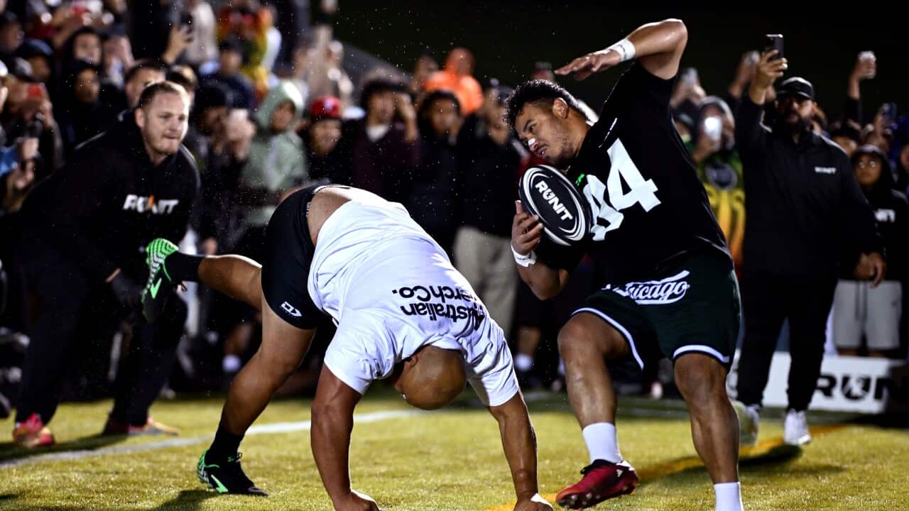 Two men, one holding a ball, are colliding with each other in a field as spectators watch.