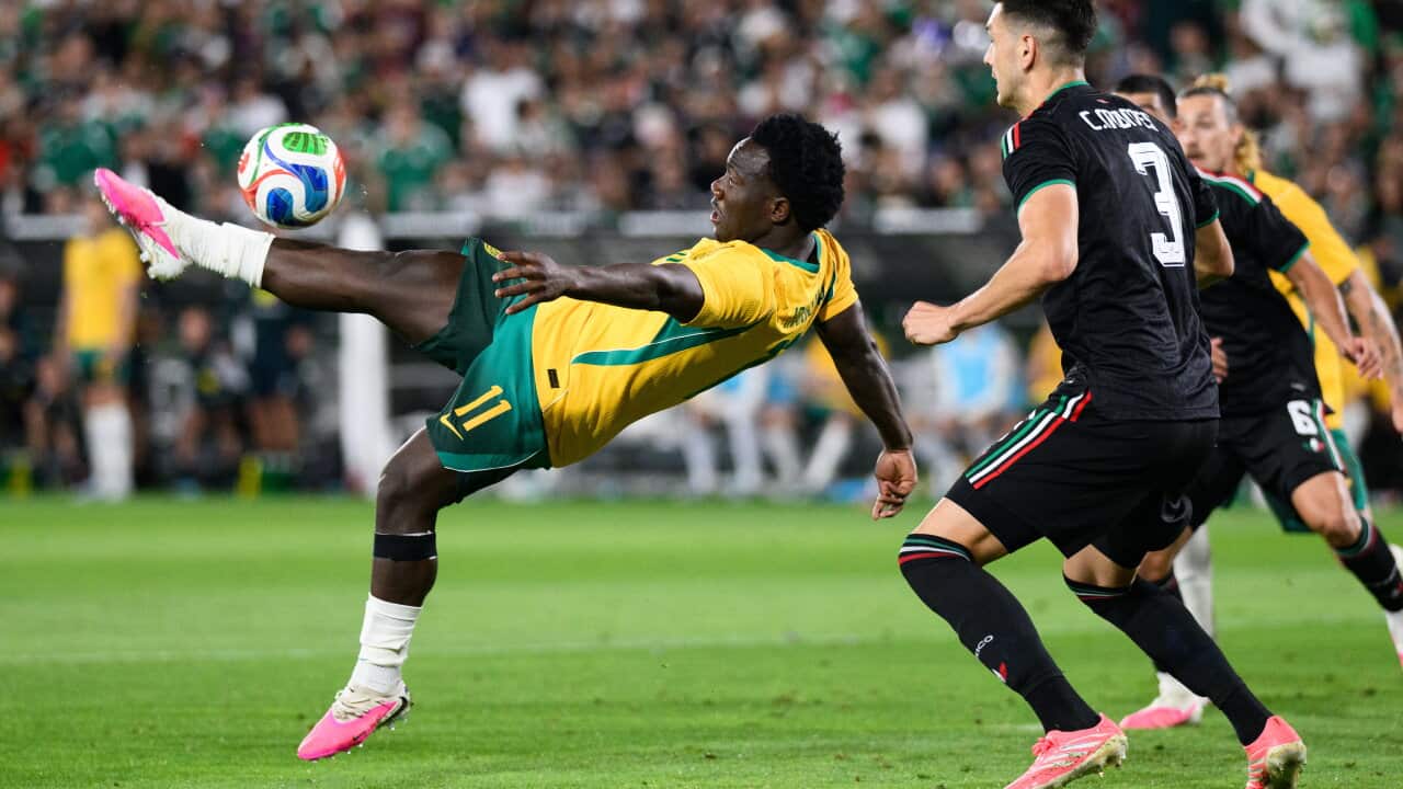 A football player in a yellow and green uniform executes a high volley kick mid-air next to an opposing player in a black jersey.