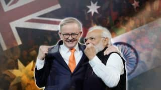 Anthony Albanese (left) and Narendra Modi raise their fists to the crowd, with Australian and Indian flags faded in the background.