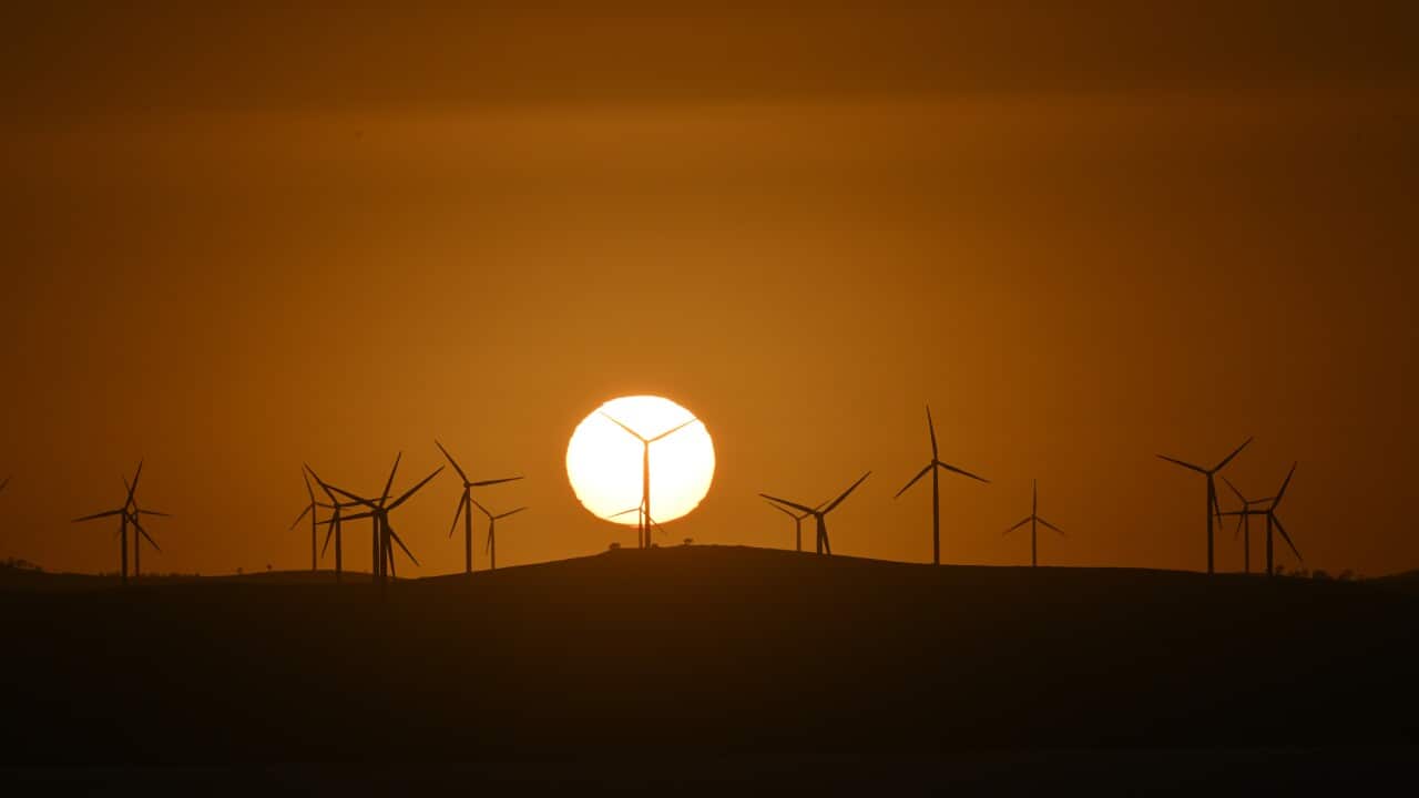 A yellow sun and an orange sky, with the outline of wind turbines on a hill.
