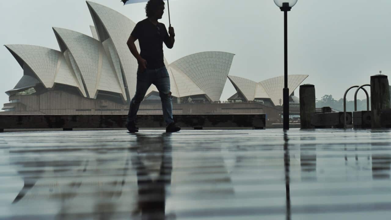 A man walks past the Sydney Opera House during a rain storm in Sydney