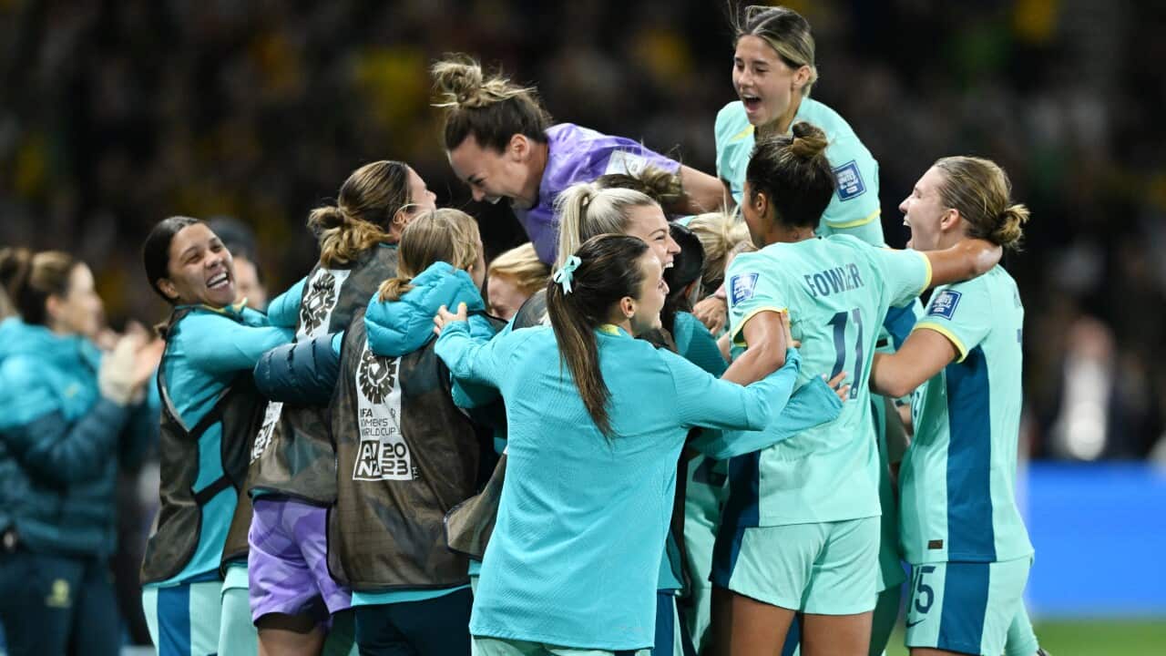 Matildas players cheering and hugging on a stadium field.