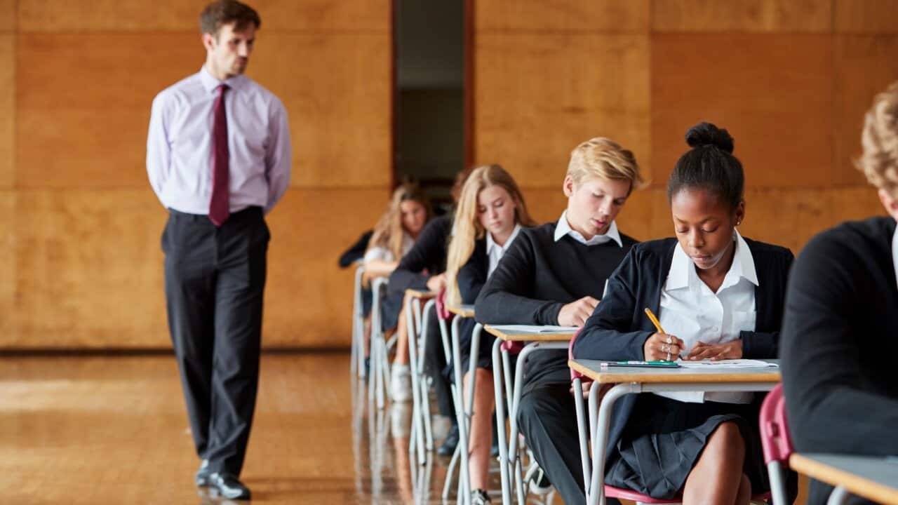 Teenage Students Sitting Examination With Teacher Invigilating