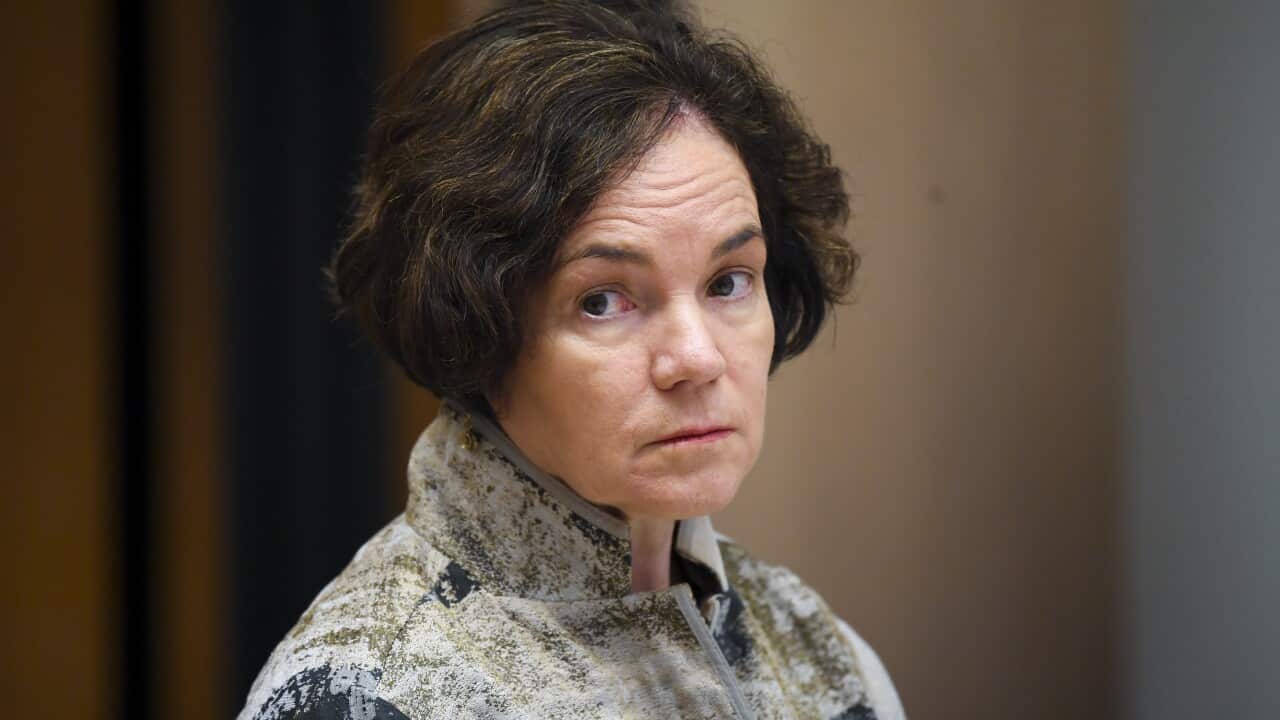 A woman wearing a blue, green and white jacket, with her eyes looking to the side.