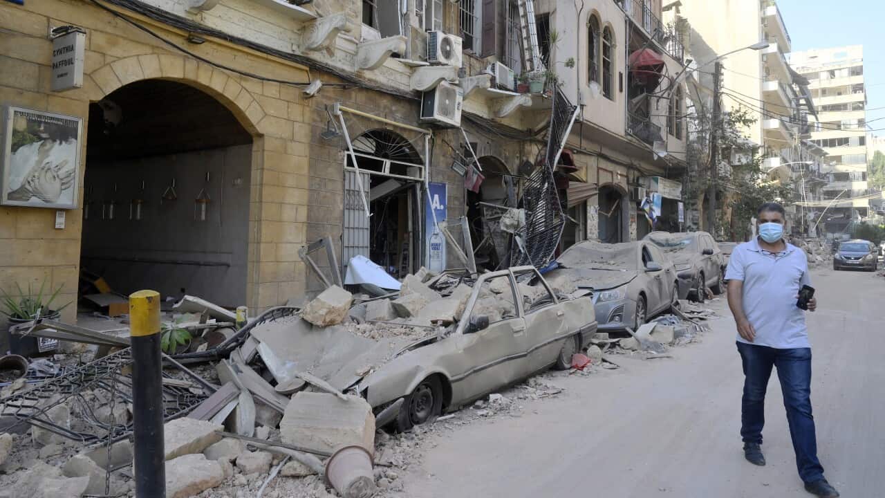 A man walks next to damaged vehicles in the aftermath of a massive explosion in Beirut.