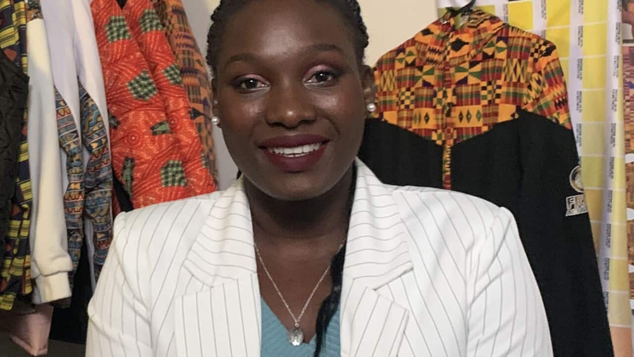 Alies Bol sits in front of a rack of brightly coloured clothing.