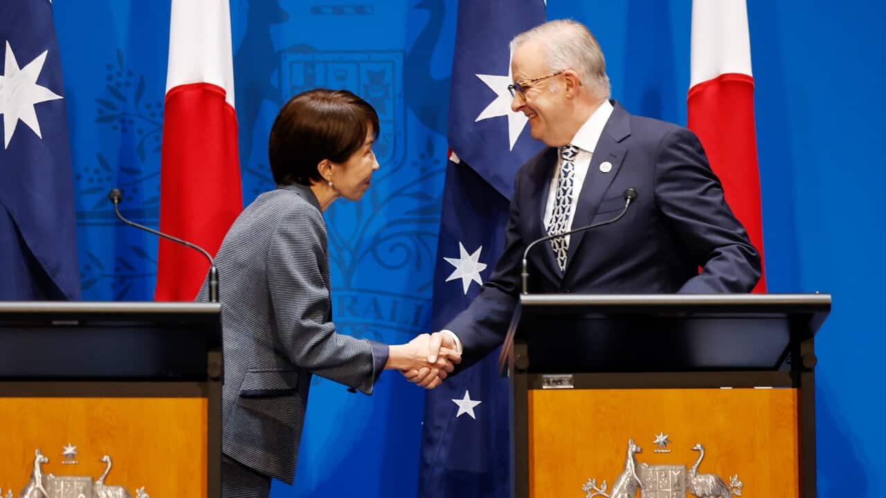 Sanae Takaichi shakes hands with Anthony Albanese in front of a row of Japanese and Australian flags.