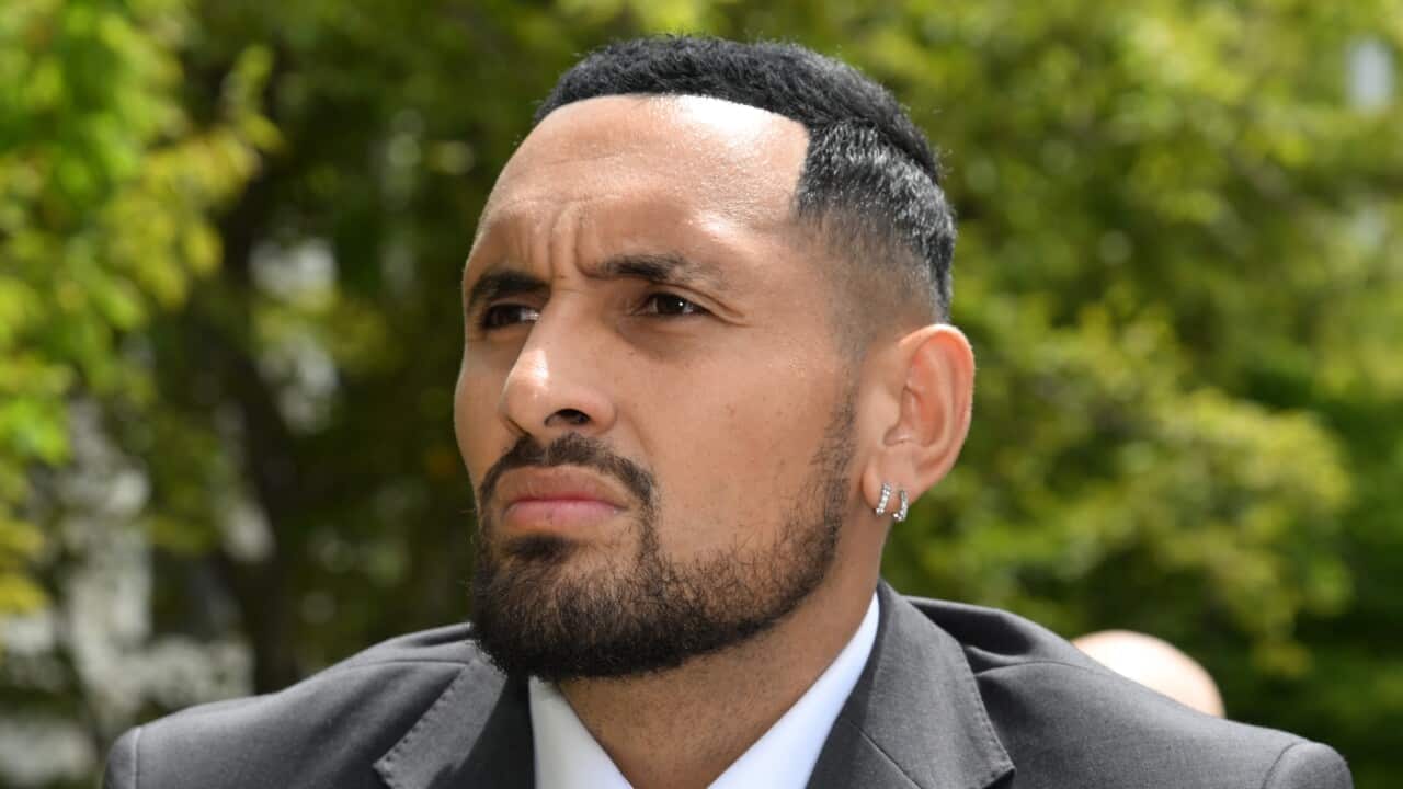 Nick Kygios in a suit, using crutches