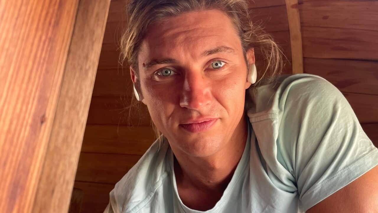 A young man with blond hair and a light blue shirt looks at the camera.