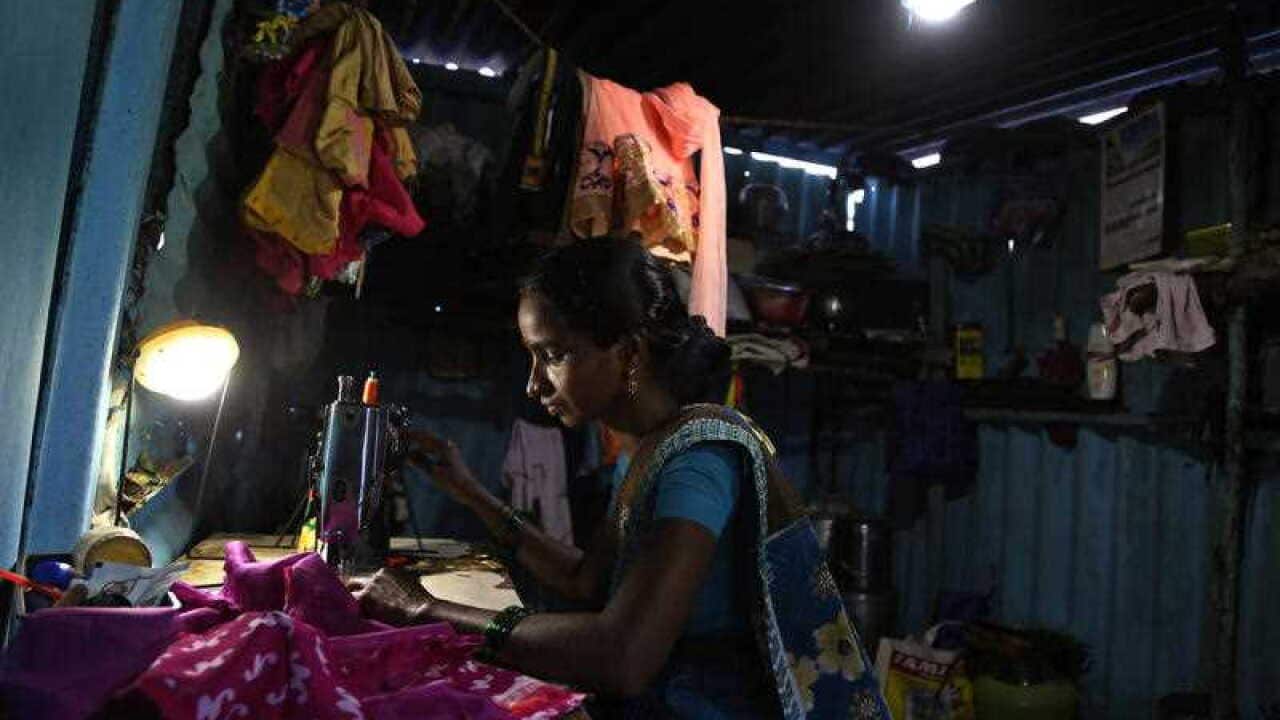 An Indian slum dweller sews clothes under the lithium battery run solar lights, provided by Pollinate Energy, a non-government organization, inside her shanty