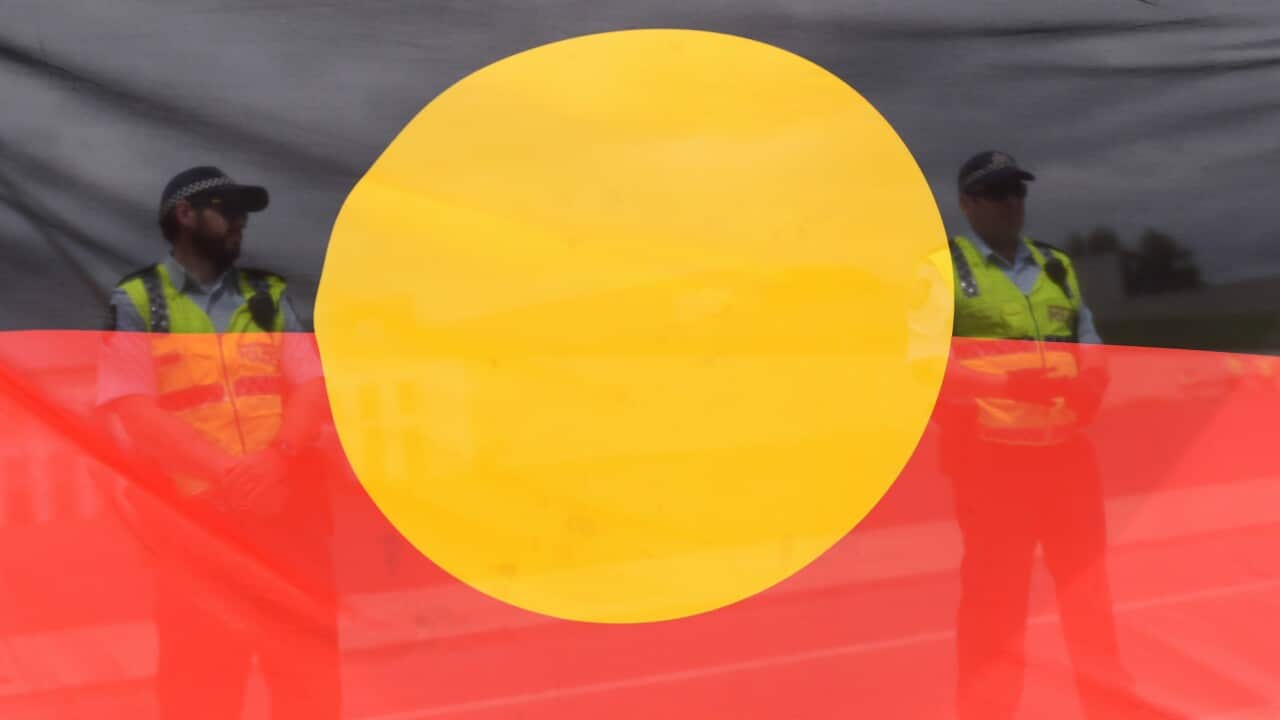 Policemen are seen standing behind an Aboriginal flag during a protest outside Parliament House in Canberra, Monday, Feb. 9, 2015. (AAP Image/Lukas Coch) NO ARCHIVING