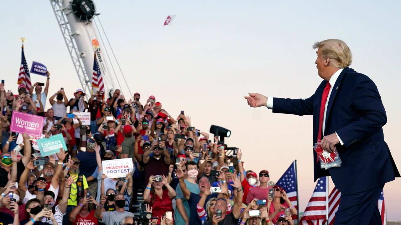 President Donald Trump throws face masks into the crowd as he arrives at the campaign rally on Monday.