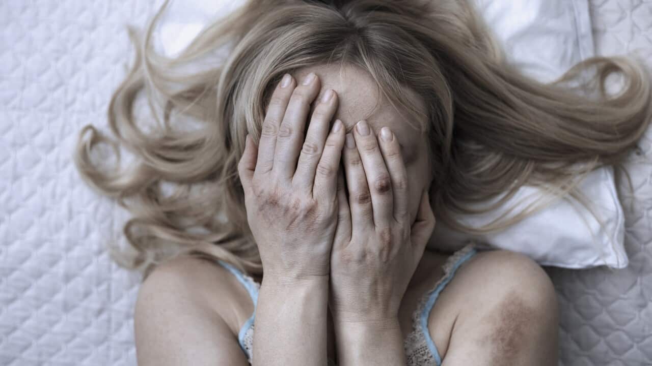 Woman covering face with hands while lying on bed at home