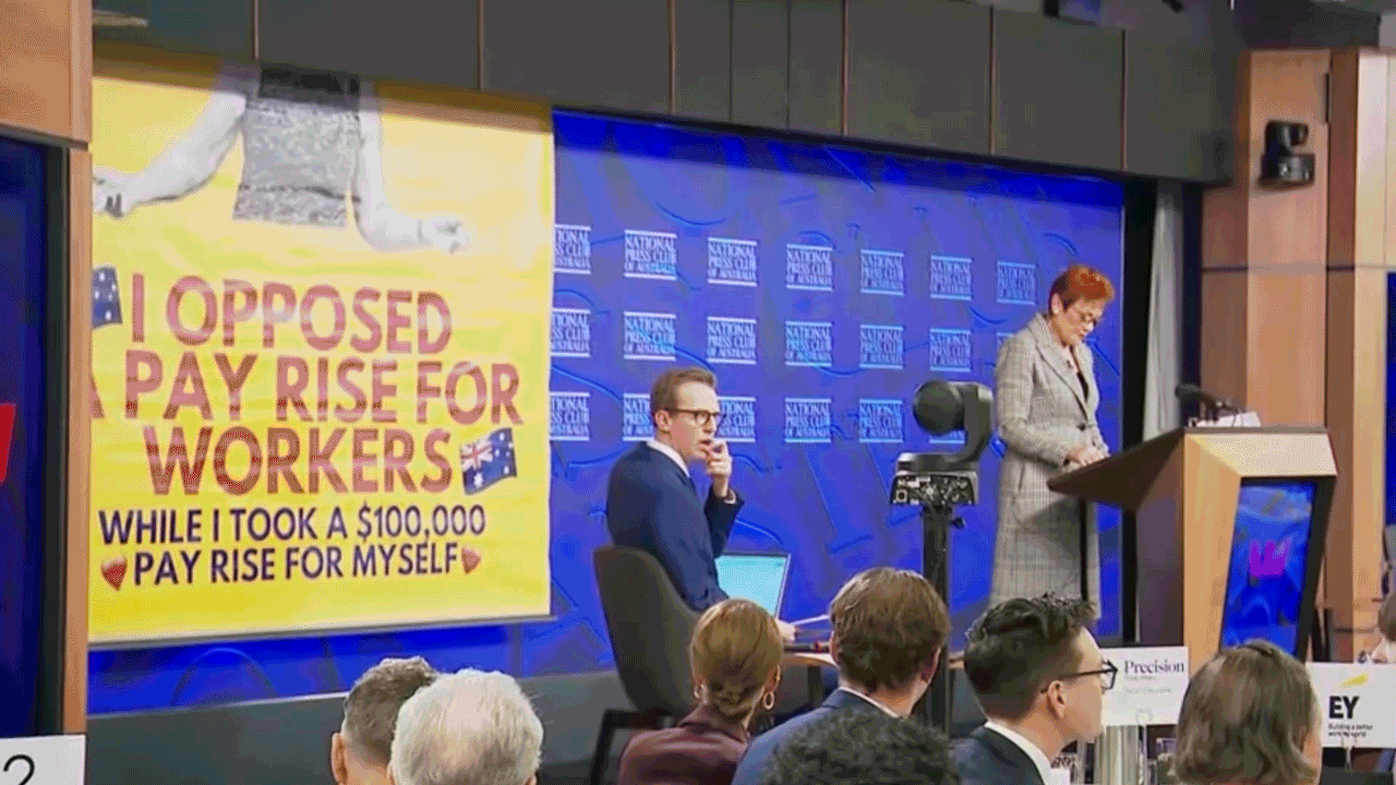 Hanson delivers a speech next to a protest banner at her Press Club address