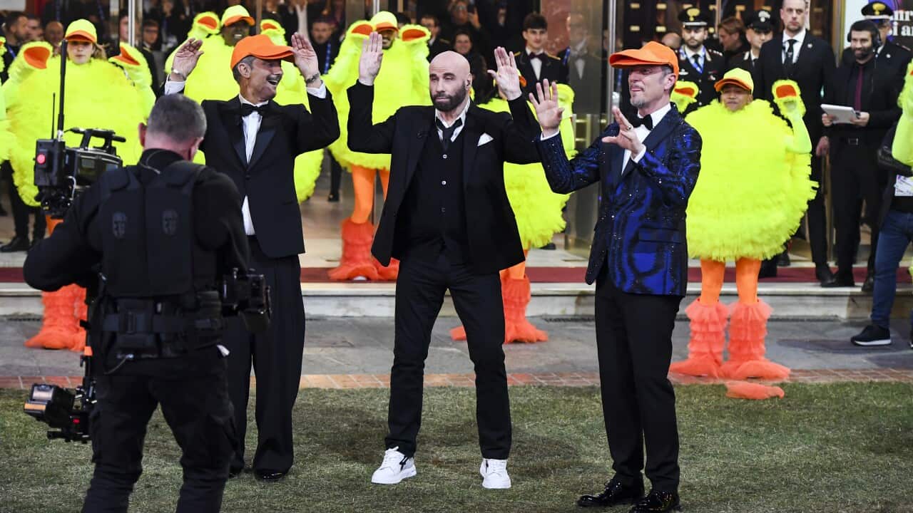 John Travolta performs the chicken dance with people dressed up as chickens.