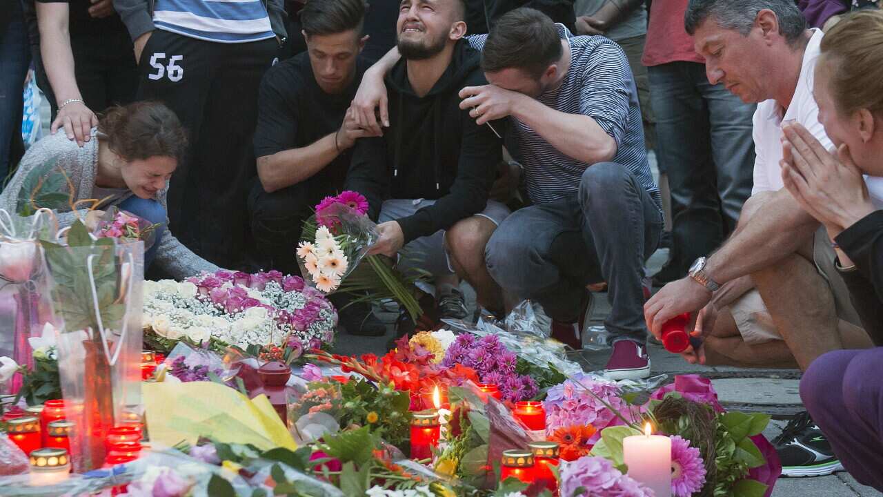 People mourn behind flower tributes near the Olympia shopping center