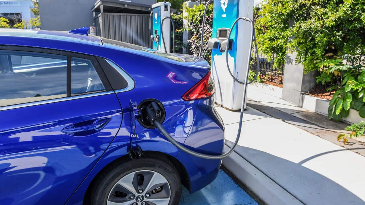 The back half of a blue sedan, with a charger connecting the car to a charging station.