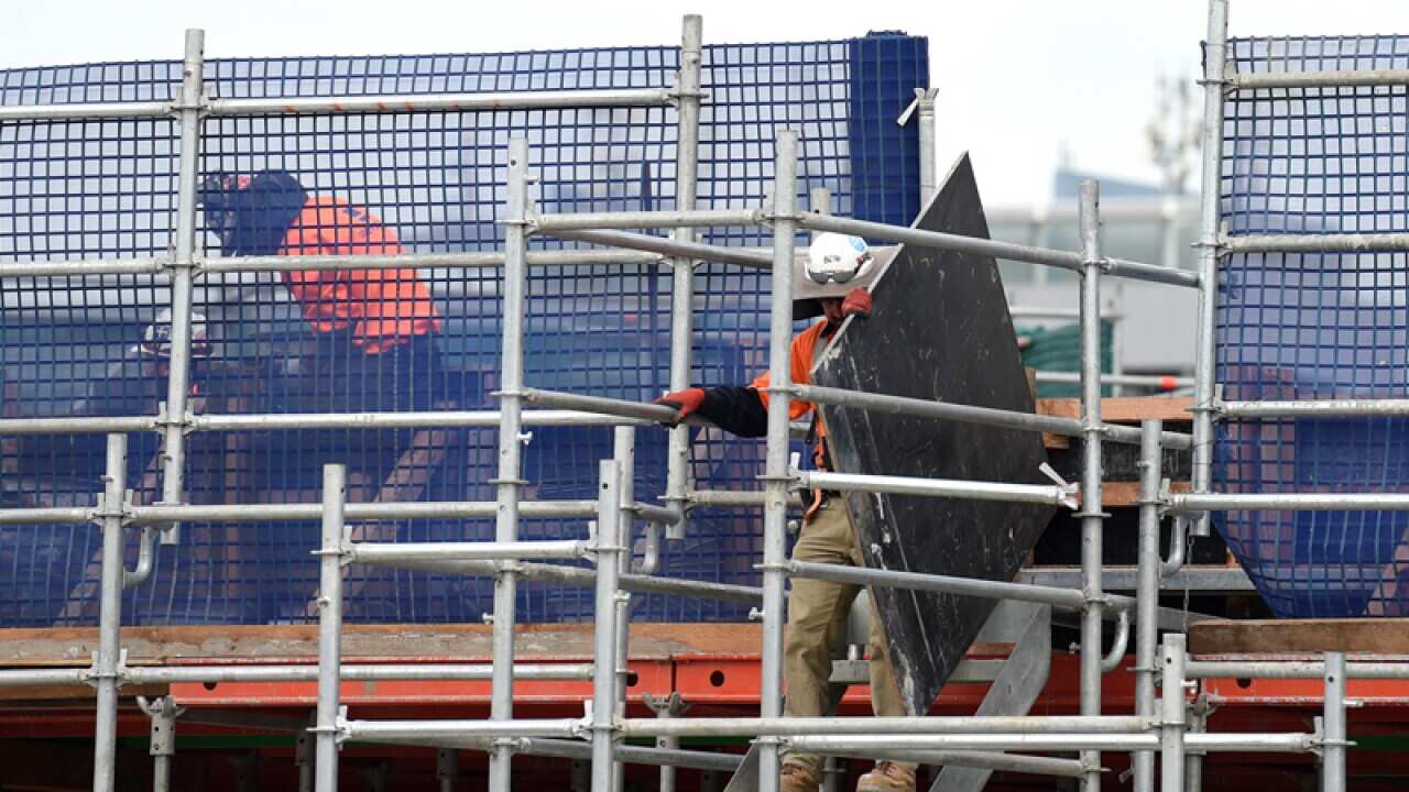 A construction worker carries a piece of wood at a work site