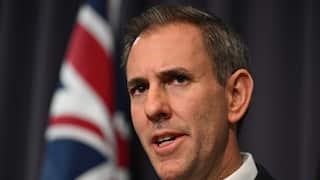 Australian Treasurer Jim Chalmers speaks to the media during a press conference at Parliament House in Canberra. The image is in closeup on Chalmer's face. Behind him, out of focus, is a furled Australian flag.