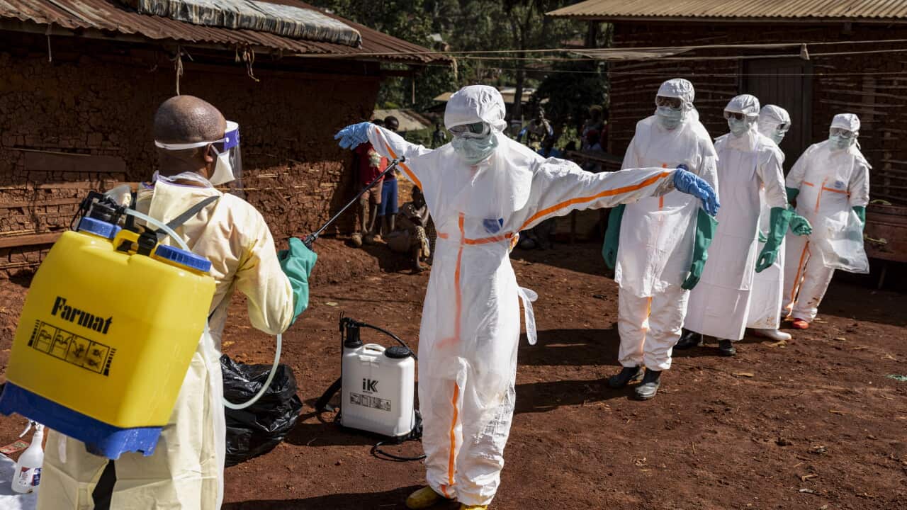 A person in white haz mat suit sprays down another person in a hazmat suit.