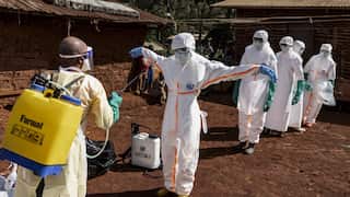 A person in white haz mat suit sprays down another person in a hazmat suit.