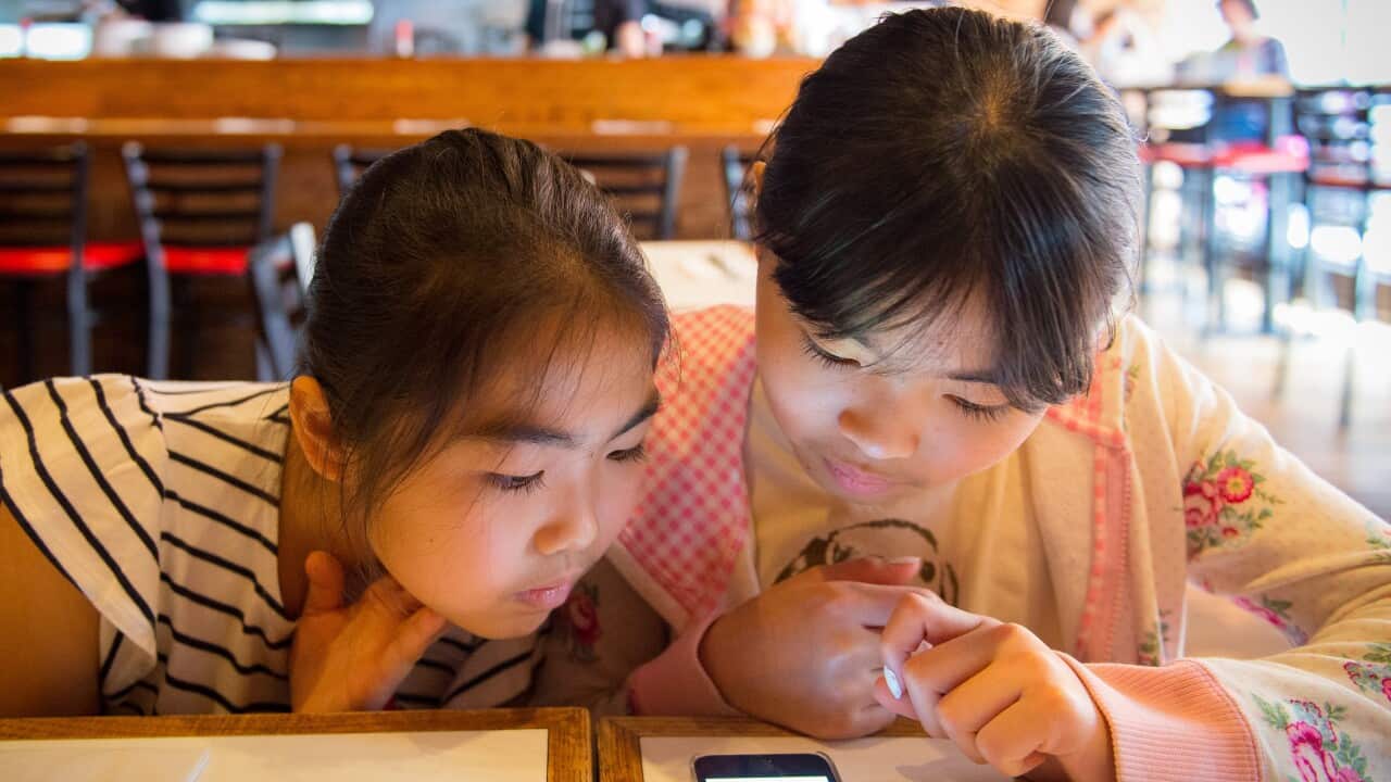 Two young children using smartphone while their food arrive at a restaurant