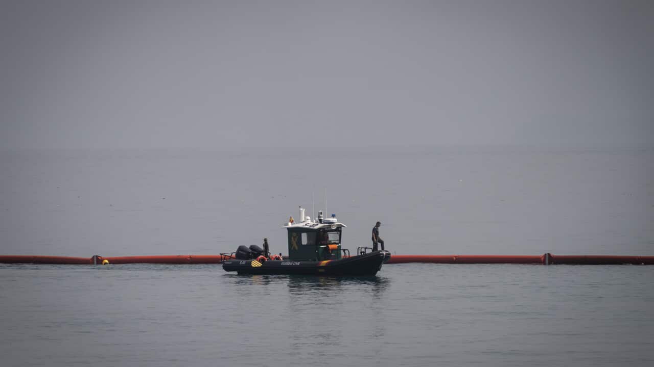 A small Spanish police boat in the sea. It is setting up a floating orange barrier on the water's surface.