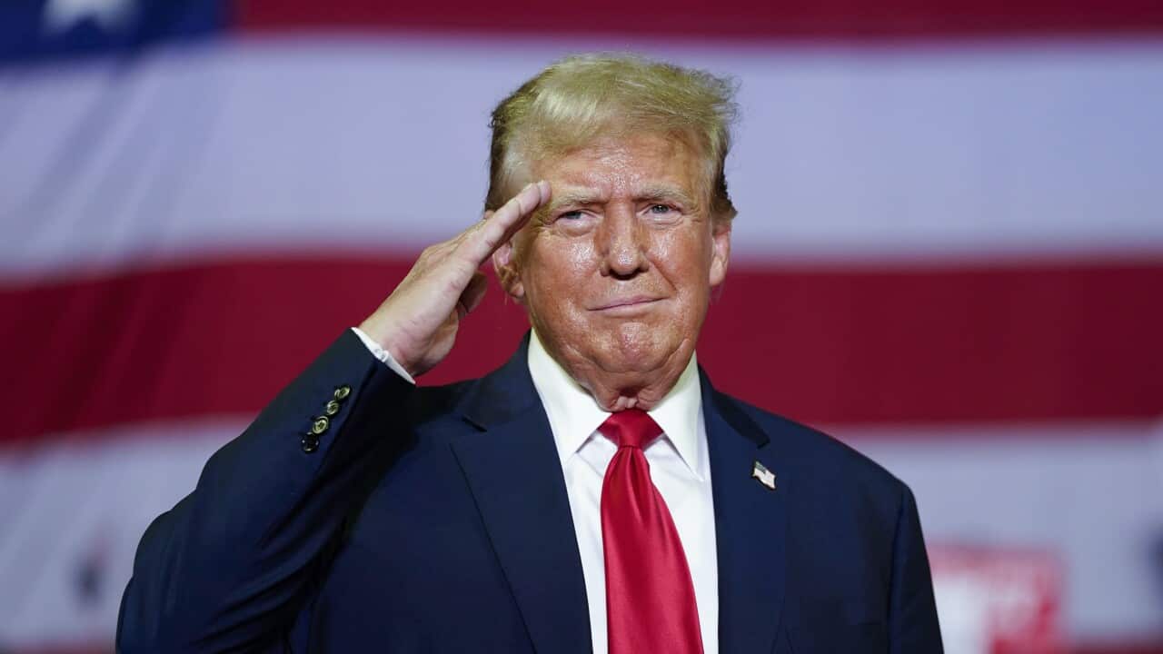 Donald Trump giving a salute in front of a giant American flag.