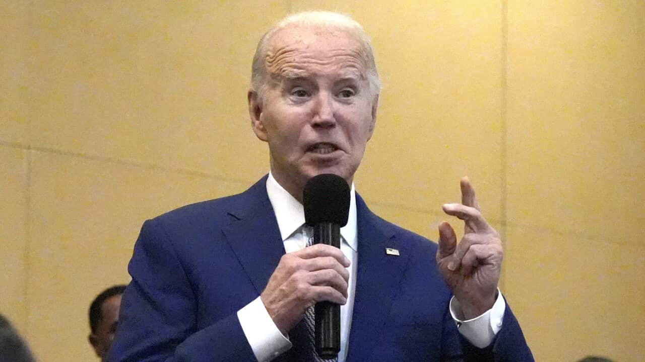 Joe Biden wearing a dark blue suit speaks into a microphone.