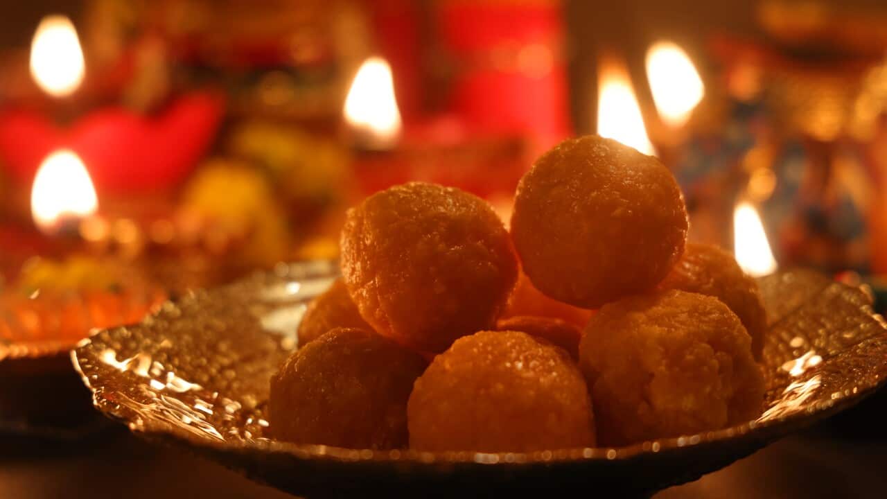 A bowl of ladoos (a traditional Indian sweet) is placed next to earthen lamps.