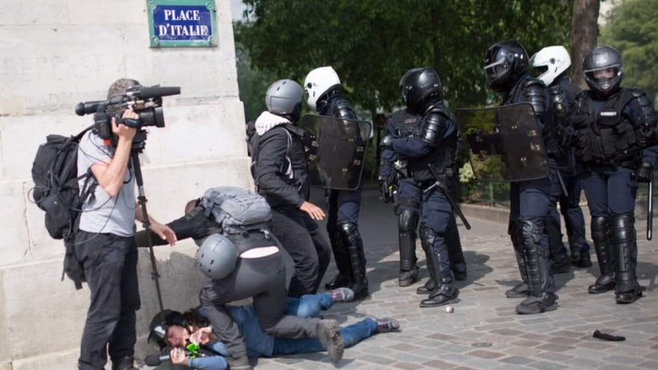 A representational image of a police wearing motorcycle helmet attack and push a women journalist holding a microphone next to her crew in Paris.