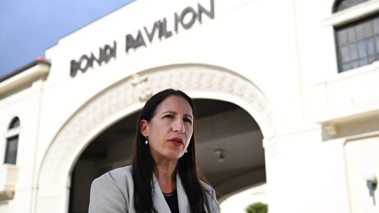 A woman with long dark hair outside a cream-coloured building with the sign Bondi Pavilion on it