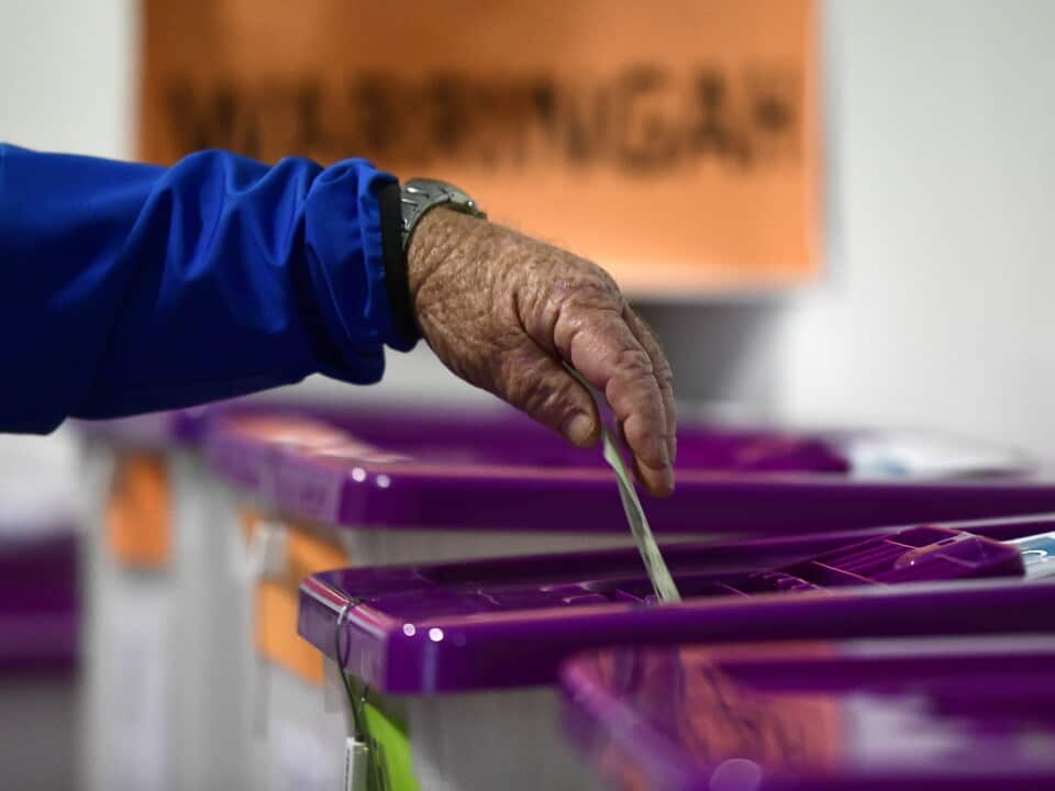 A hand puts a ballot in a box.