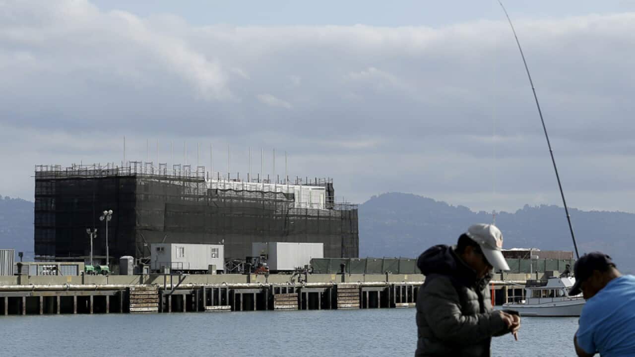 Two men fish in the water in front of a Google barge