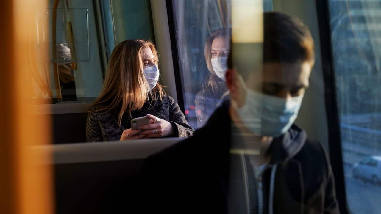 young woman sitting in train wearing protective mask, using smartphone
