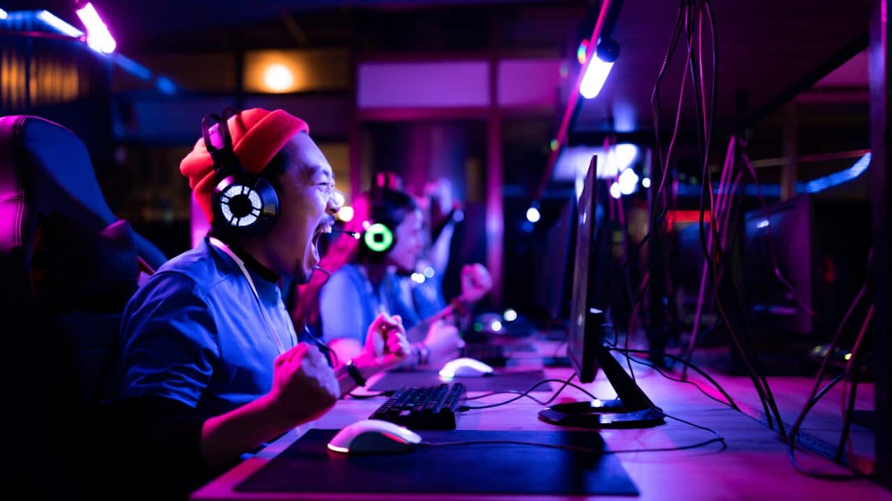 Cheerful Asian gamer celebrating his victory in eSports video games at gaming club.