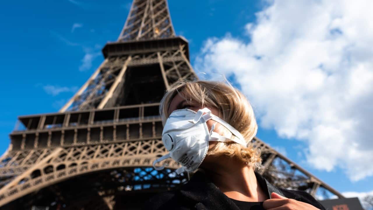 A woman with a face mask in front the Eiffel Tower in Paris.