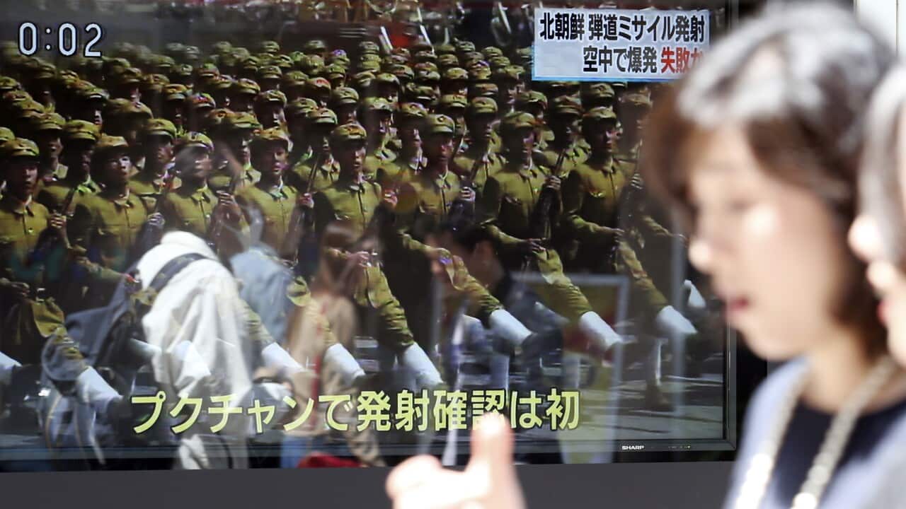 People in Tokyo walk past a TV news report showing an image of North Korean troops.