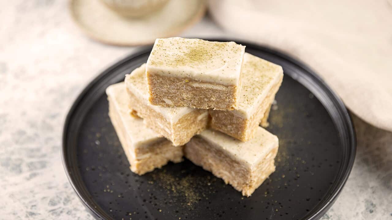 A three-deep stack of slice pieces sits of a flat black plate. Each piece of light brownish-caramel coloured slice is toped with pale icing.