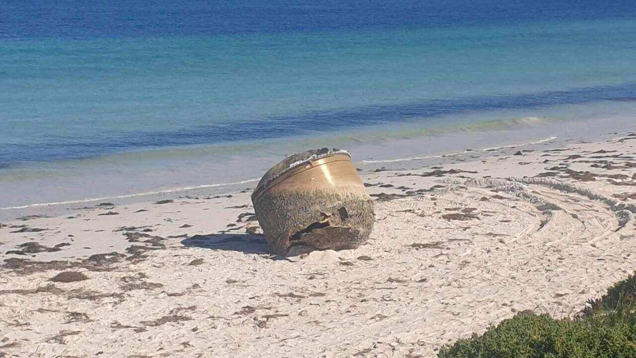 A large canister on the white sand of a beach with the ocean in the background.