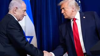 Two older men in dark suits shake hands.