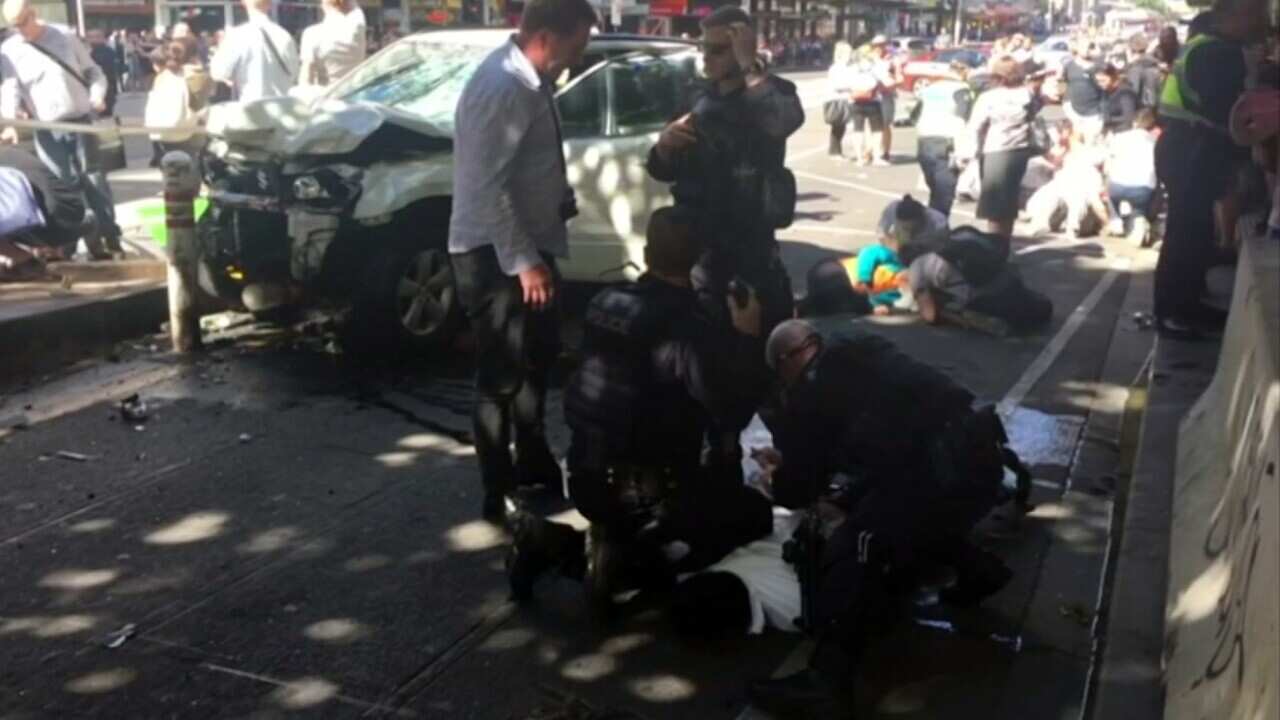 In this image taken from video made available by Lachlan V, a man is held by police after a car was driven into pedestrians on a busy Melbourne intersection.