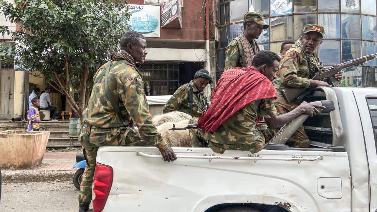Men with army uniforms and guns ride on the back of a utility vehicle