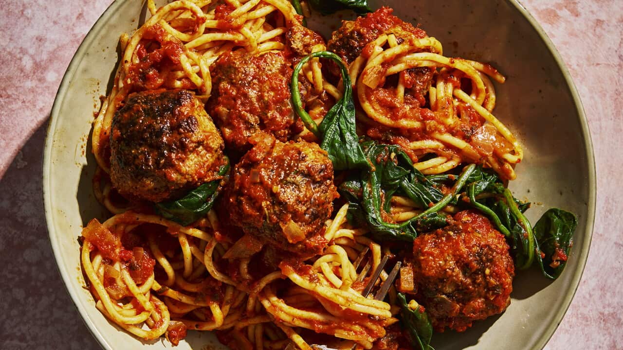 Spaghetti, meatballs and greens sit in a pottery bowl.