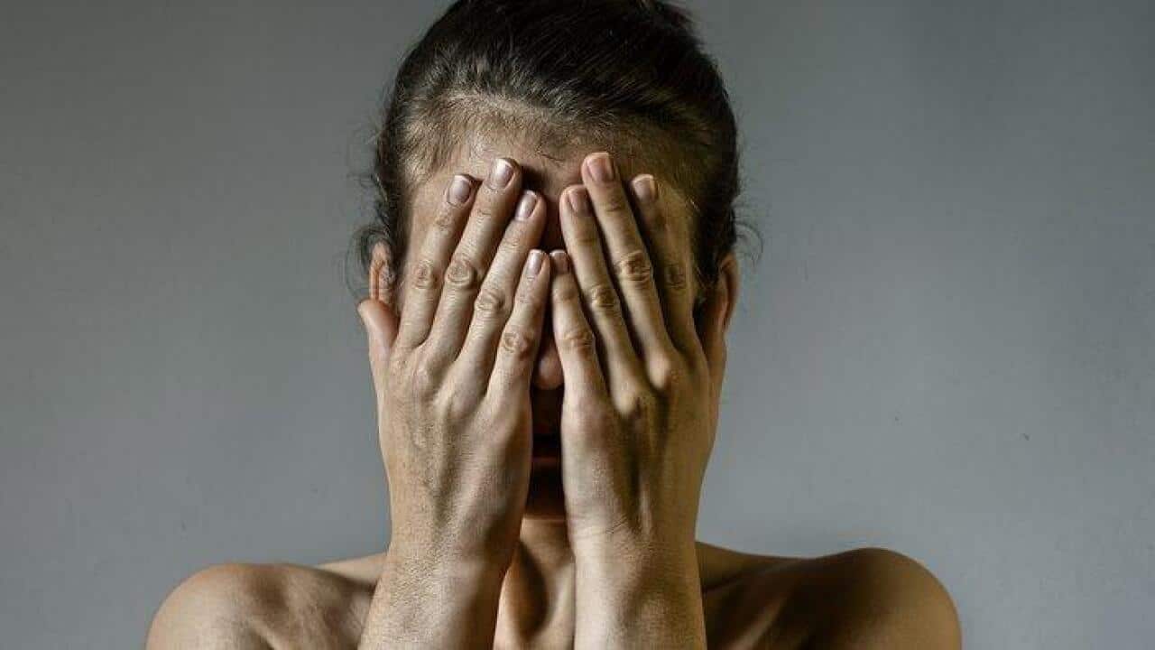 Concept of fear, shame, domestic violence. Woman covers her face her hands on scratched background.