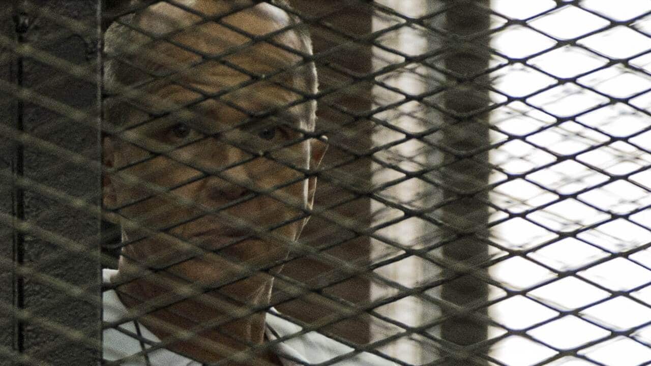 Australian journalist Peter Greste stands inside the defendants cage .jpg