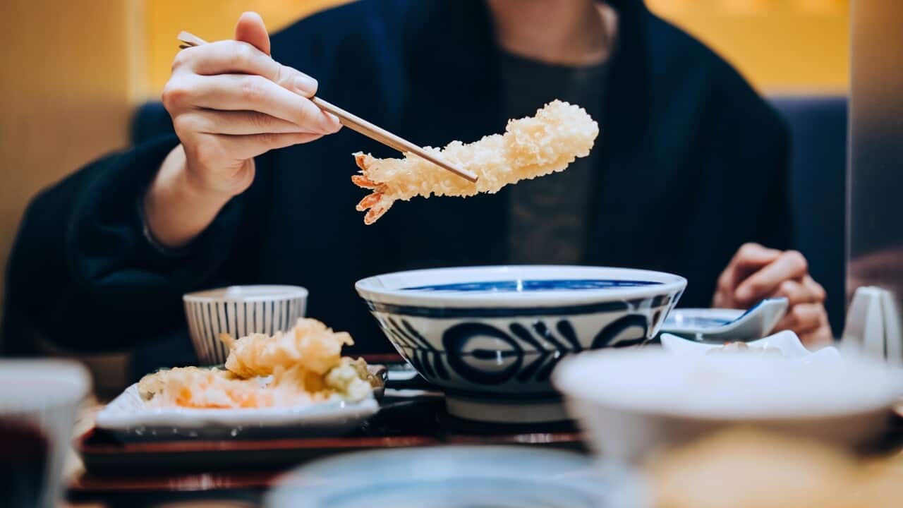 Cropped shot, mid-section of young Asian woman dining in a Japanese restaurant, enjoying delicate freshly served Japanese cuisine, seafood tempura on the dining table. Asian cuisine and food culture